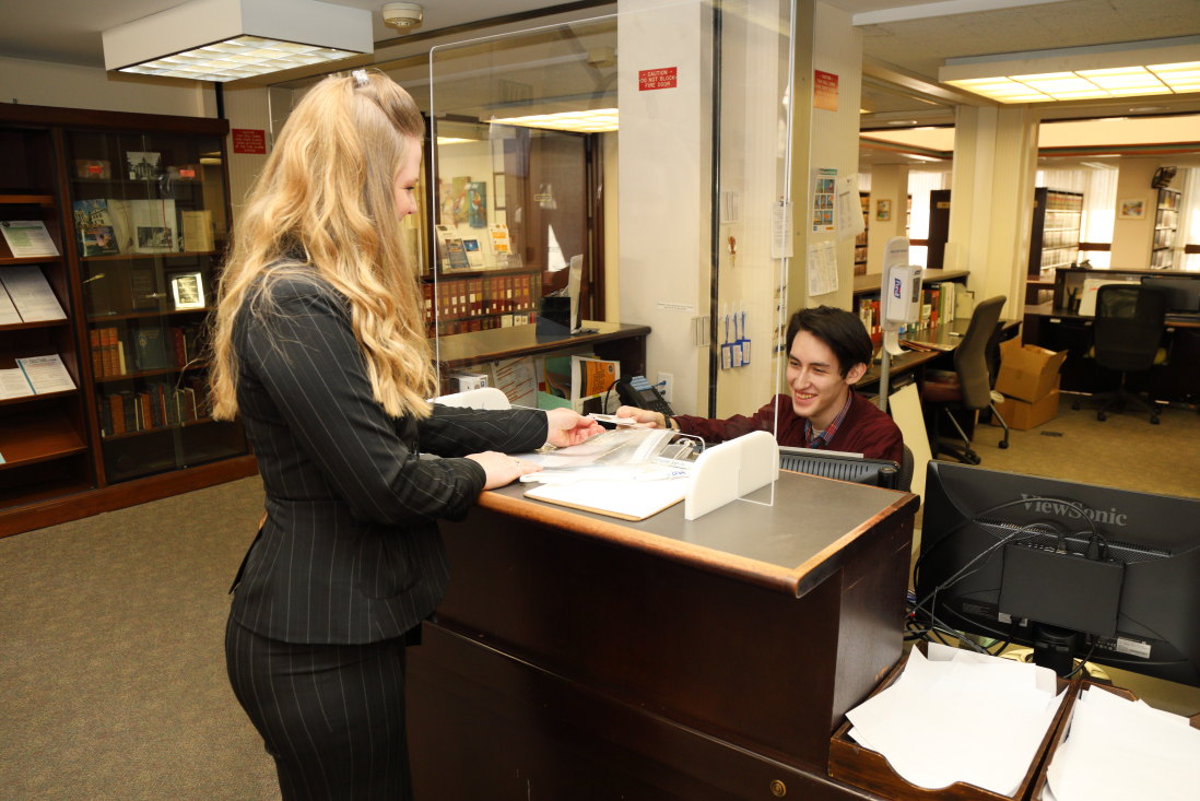 Photograph of a man at a library information desk handing a woman a library card