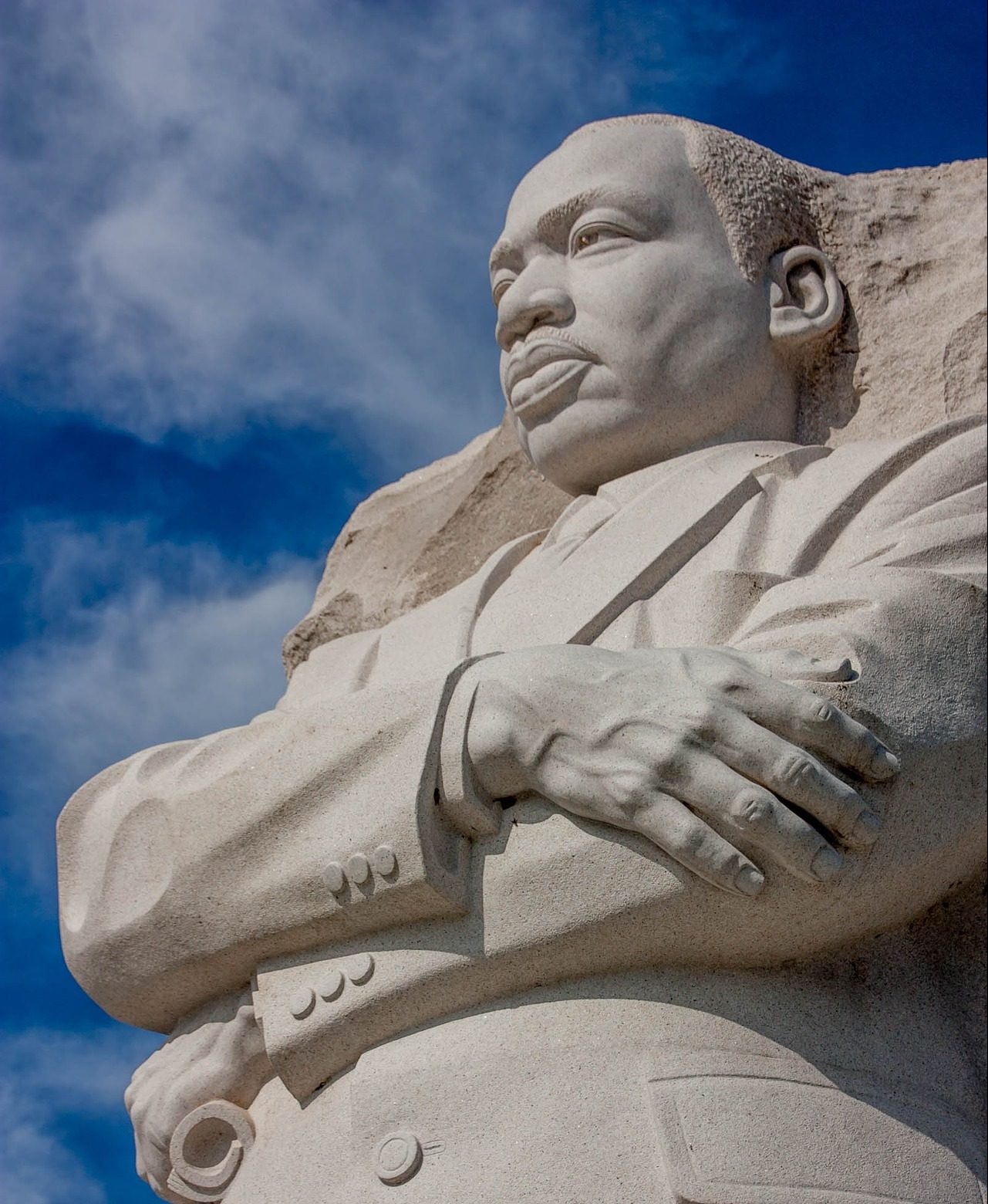 MLK memorial white granite statue in Washington DC- MLK waist up with arms crossed and blue sky in the background