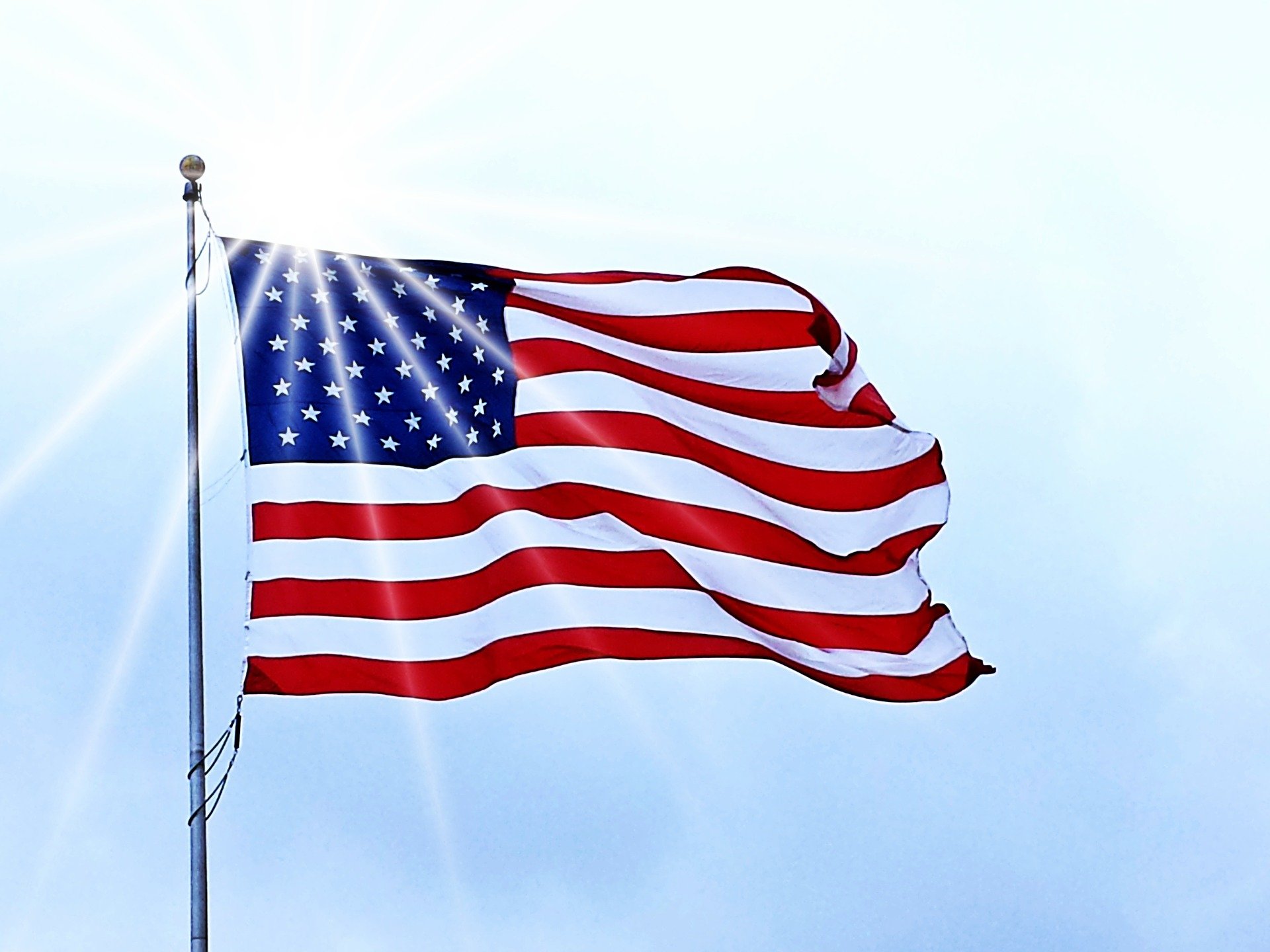 an american flag fluttering in the wind with the sun directly behind it
